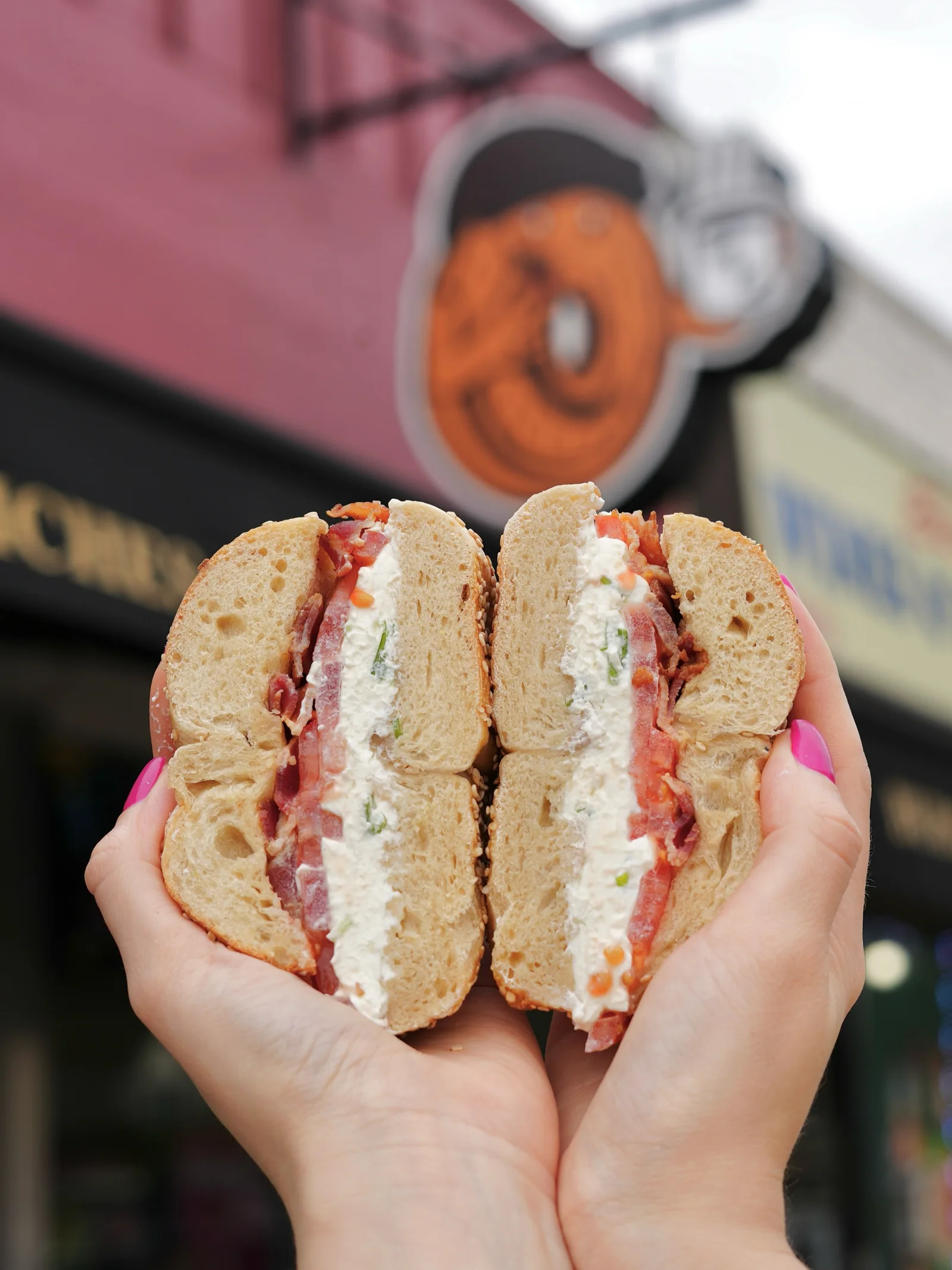 Bacon, tomato and chive cream cheese on a sesame bagel, held outside Middle Village Bagels